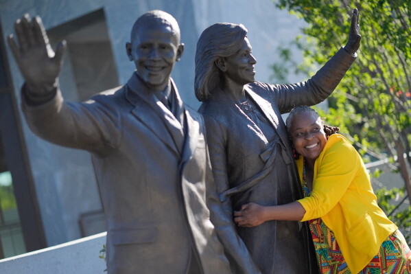Sonya Hankerson, from Ft. Lauderdale, Fla., hugging the statue of former President Barack Obama and former first lady Michelle Obama as she visits the Obama Presidential Center on the official opening, Friday, June 19, 2026 in Chicago. (AP Photo/Pablo Martinez Monsivais)