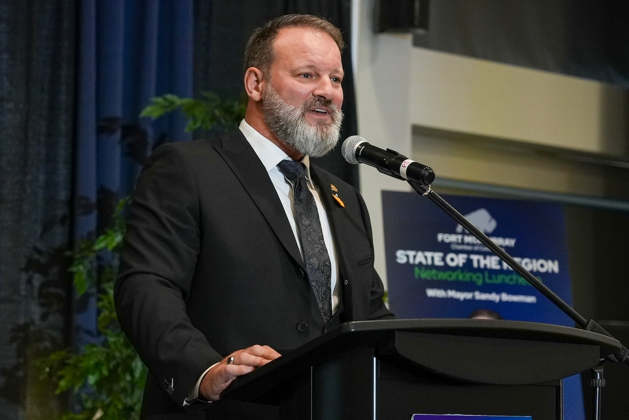 A man sitting in a suit speaks at a podium