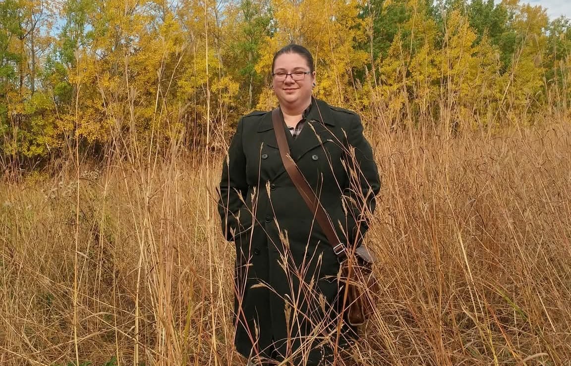A woman stands in a field of tall grass.