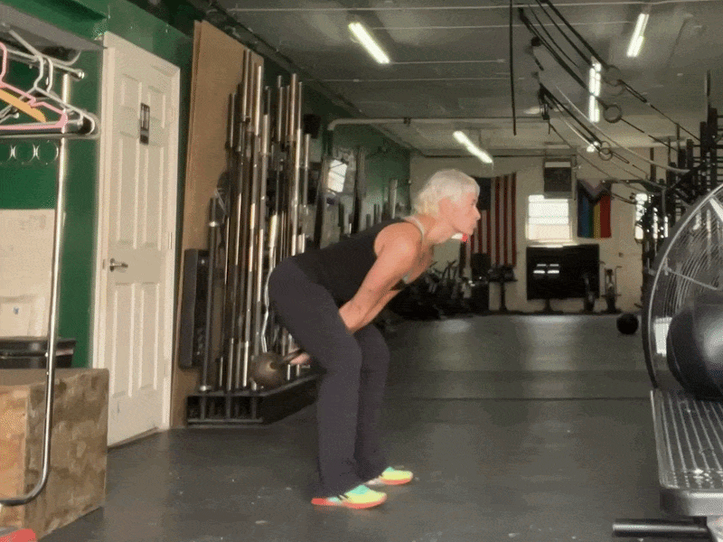 This is a photographic GIF showing a kettlebell swing exercise. In this exercise, stand with your feet shoulder-width apart and hold a kettlebell with both your hands. Use an explosive hip thrust to swing the kettlebell between your legs and back up to about chest height.