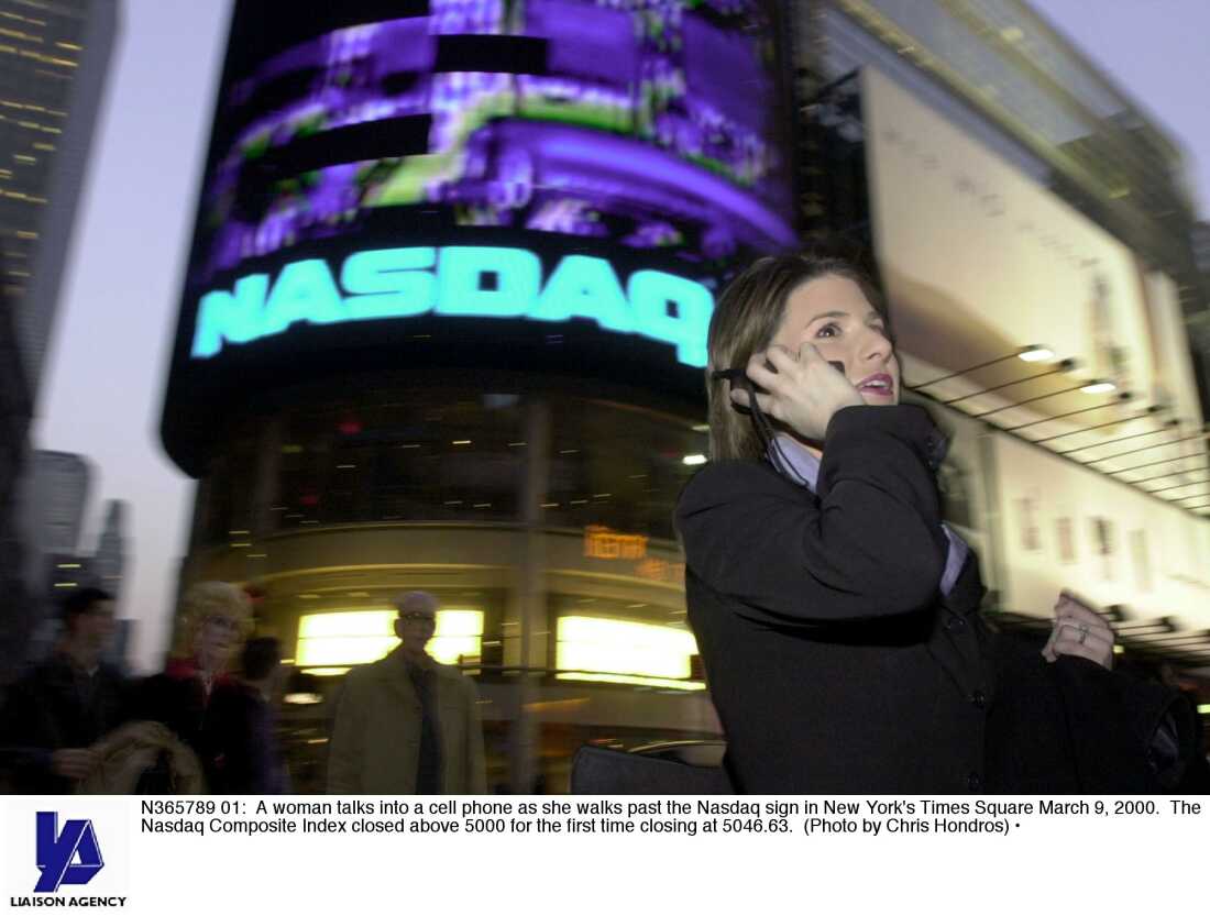 In this photo from 2000, a woman holding a cellphone to her ear walks past the illuminated Nasdaq sign in New York City's Times Square.