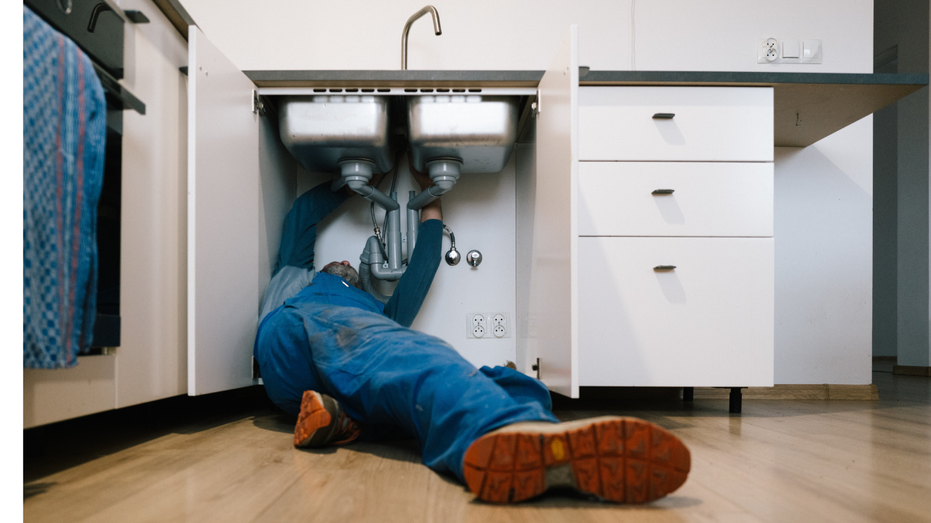 A plumber fixes a sink in a house.