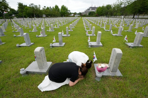 South Korean Jang Eun-jin, bottom, and her daughter Lee Beom bow in front the grave of her grandfather Jang Jae-hong who fought during the Korean War to mark the 76th anniversary of the outbreak of the Korean War at the National Cemetery in Seoul, South Korea, Thursday, June 25, 2026. (AP Photo/Ahn Young-joon)