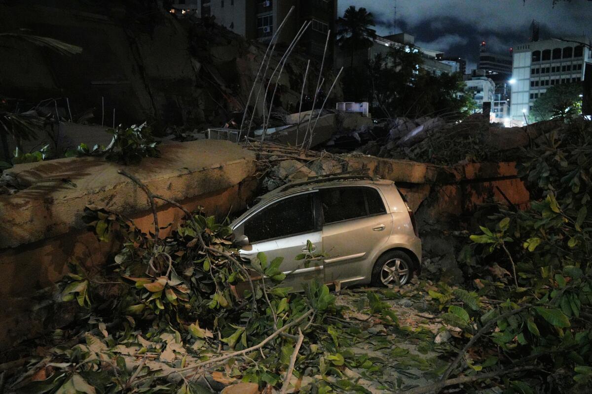 A silver-colored car is trapped under the rubble of a building