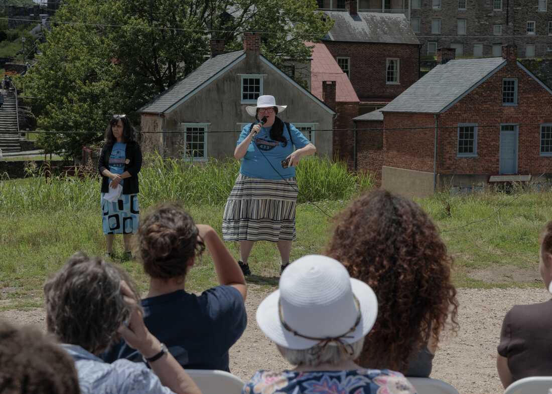 Former National Park Ranger Melissa Dalley, 49, seen here holding a microphone in front of a crowd, speaks during the America 433+ teach-in at Harpers Ferry National Historic Park on June 19, 2026. 