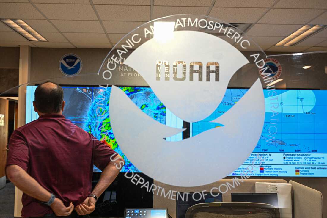An employee standing with his back to the camera looks at multiple hurricane models displayed on large screens at the National Oceanic and Atmospheric Administration's National Hurricane Center in Miami on May 30, 2025.