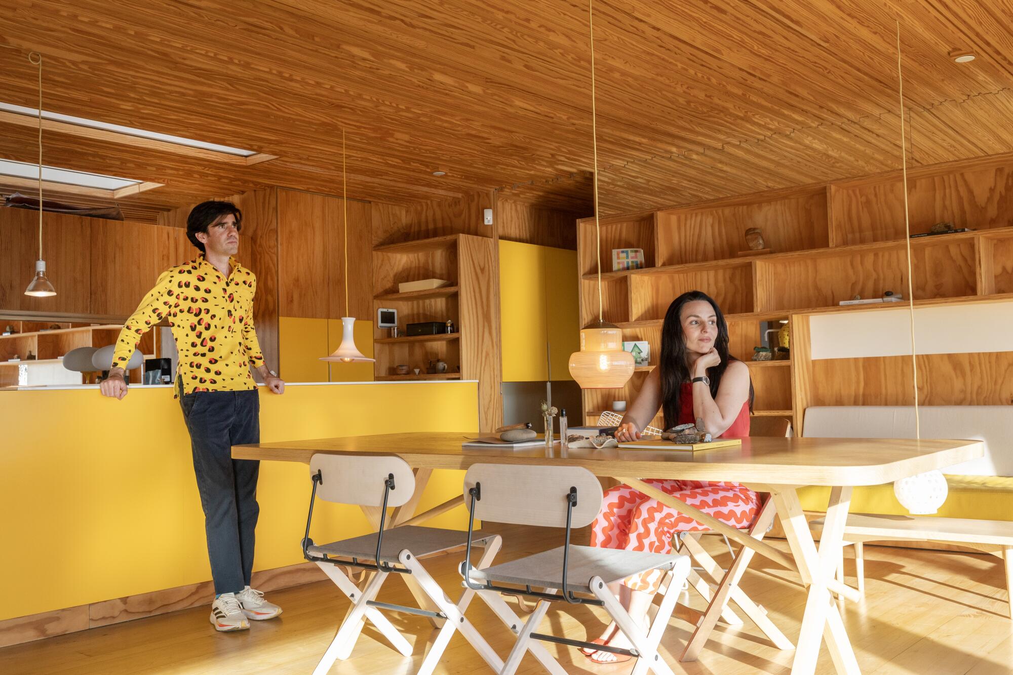 Two people in the living area with warm wood and yellow island.