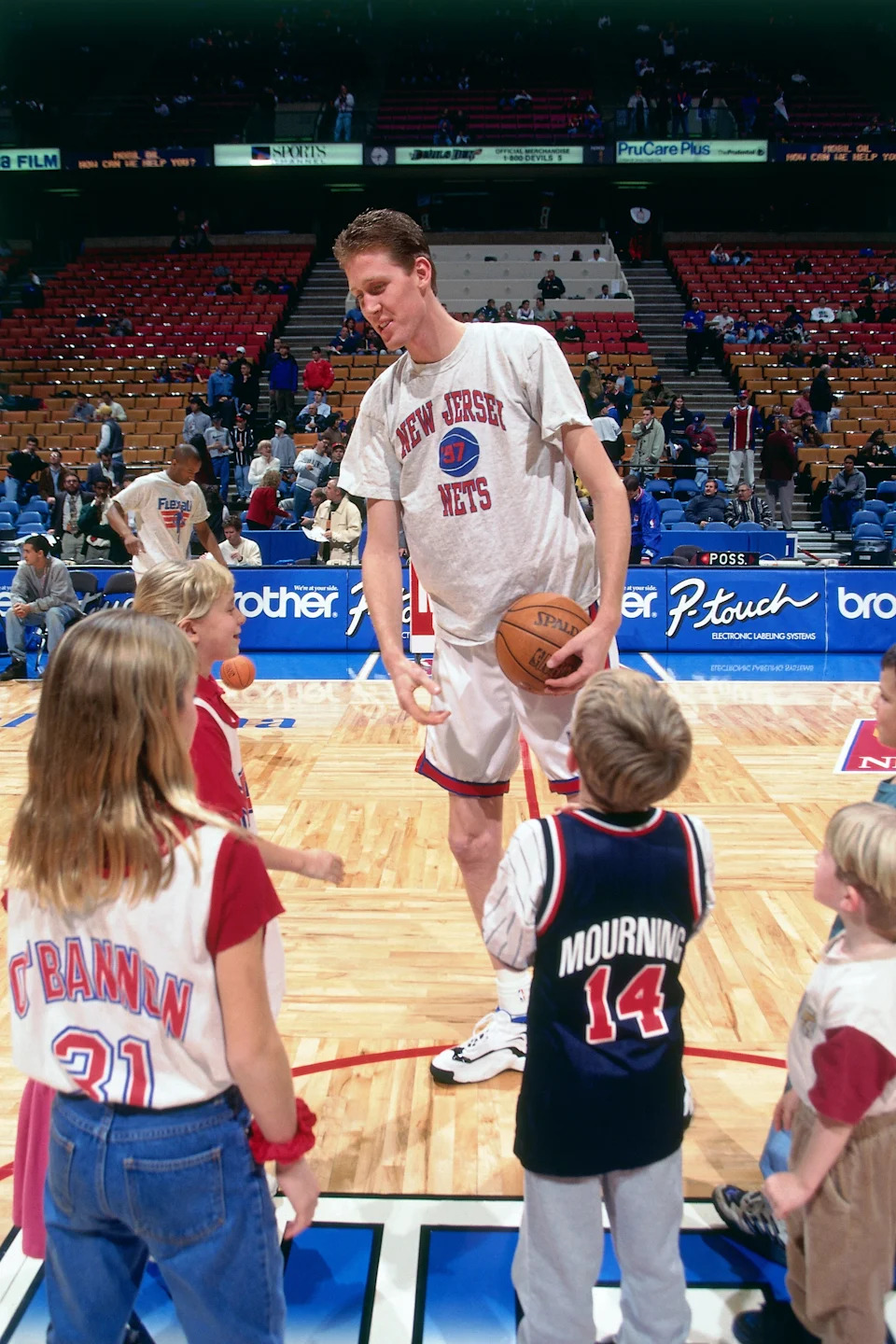 Basketball player in a New Jersey Nets shirt interacts with young fans on a court during a pre-game or halftime event