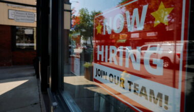 A "Now Hiring" sign hangs in the window of a hair salon in Medford, Massachusetts
