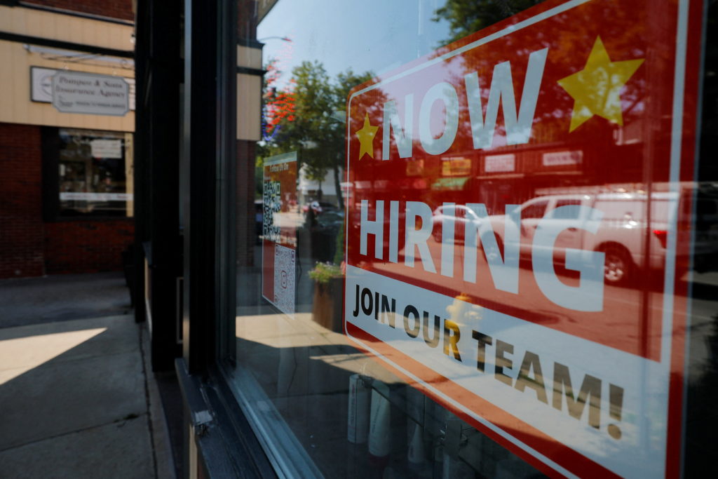 A "Now Hiring" sign hangs in the window of a hair salon in Medford, Massachusetts