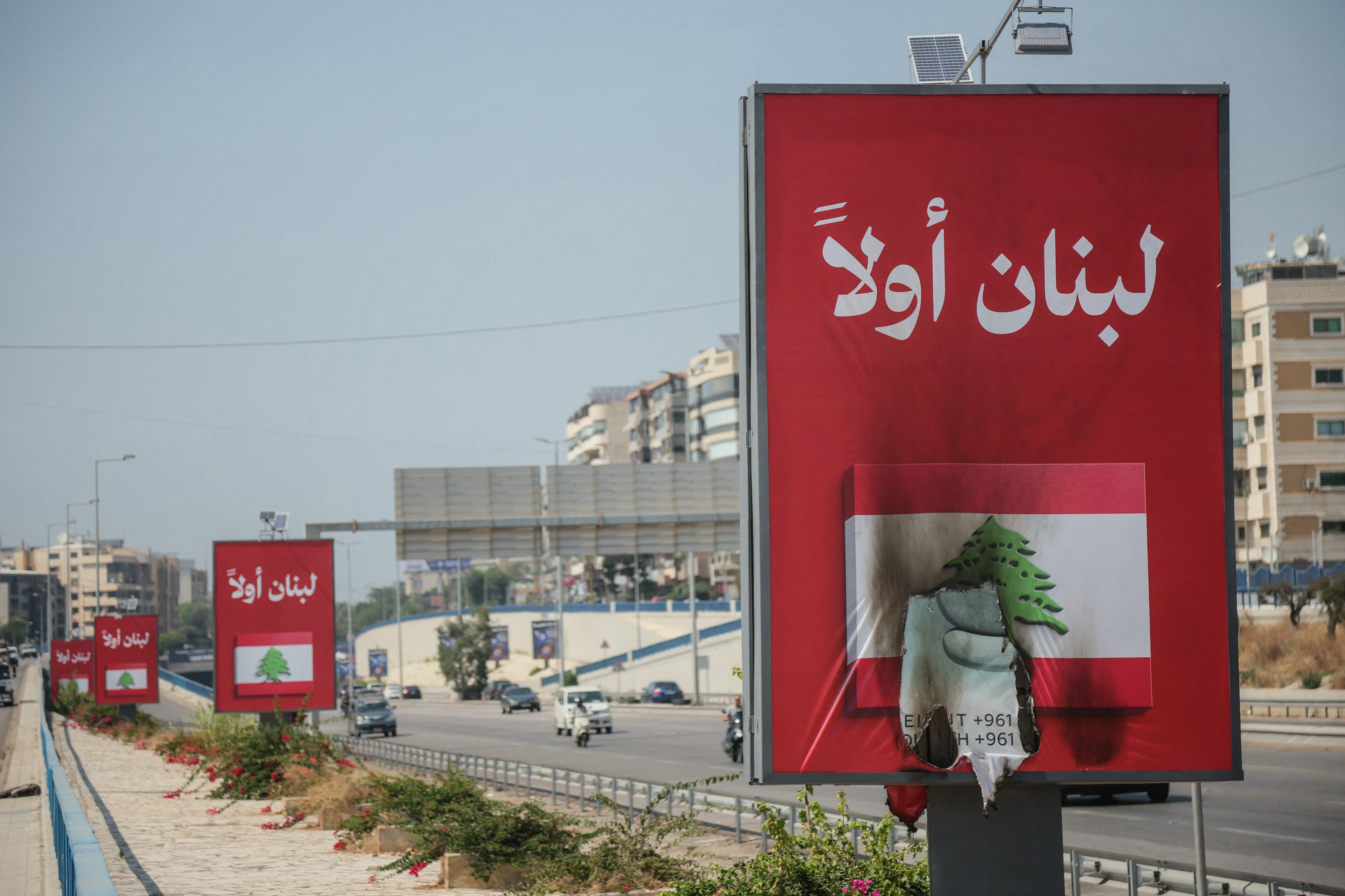 Vehicles drive past billboards that read in Arabic, Lebanon first, one of which has been set on fire along Beirut's airport road near Tehran-backed Hezbollah's stronghold, amidst tensions following Lebanon's framework agreement with Israel on 28 June 2026
