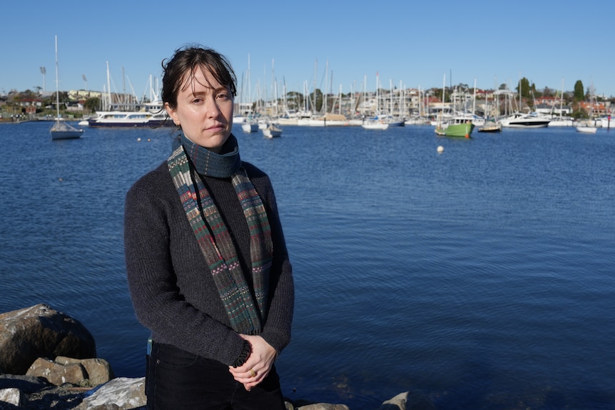 A woman stands in front of a waterway with yachts behind her.