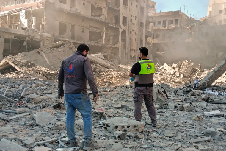 Civil defense workers inspect rubble from destroyed buildings outside