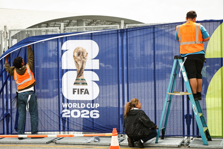 Workers affix FIFA World Cup 2026 logos and signage on a fence outside of SoFi Stadium
