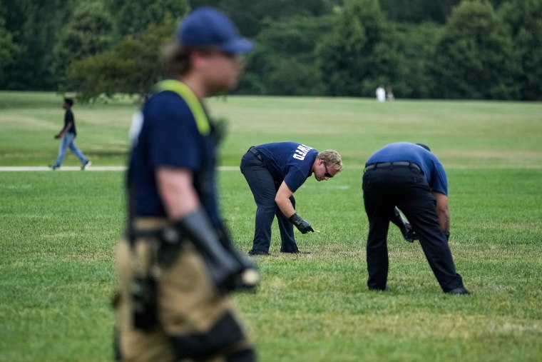 Law enforcement officials bent at the waist and examining the lawn in the National Mall.