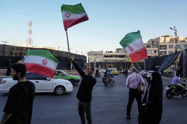 Iranians waving national flags in the street at sunset.