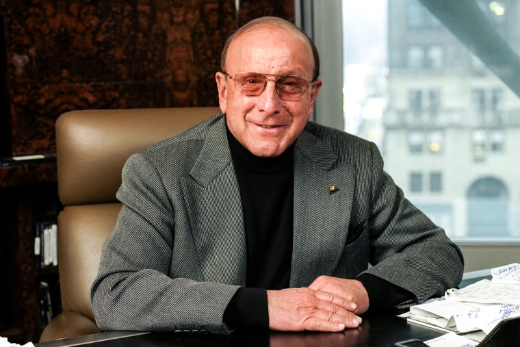 Clive Davis sits at a desk in an office by a window