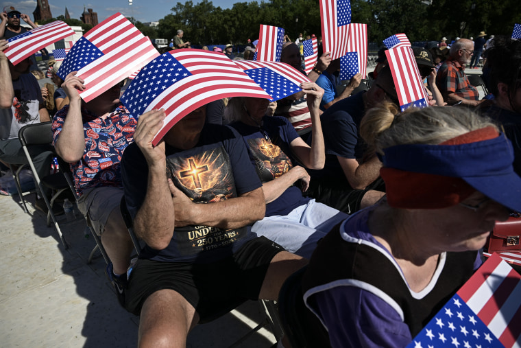 People sheltering from the sun under cardboard American flag signs.