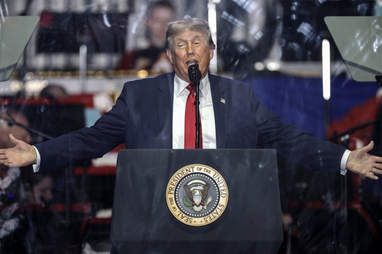 President Trump holds both hands out while speaking at a lectern.