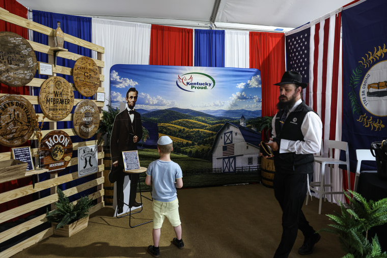 A boy stands in front of a cardboard cutout of Abraham Lincoln in a booth decorated in red, white and blue.
