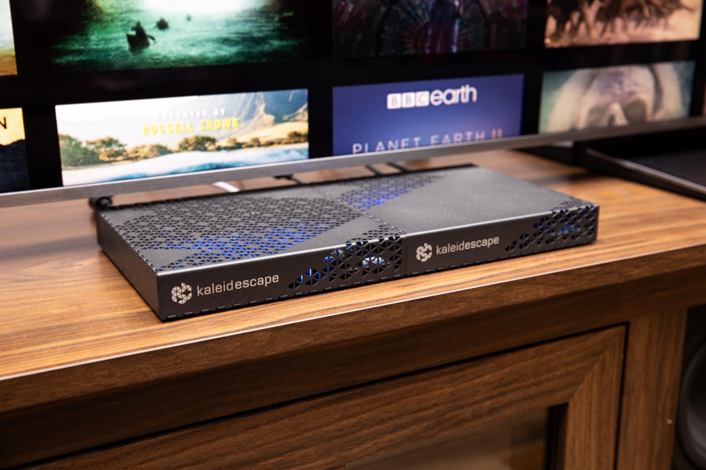 A Kaleidescape Strato E player next to a Mini Terra Prime server on a wooden home theater credenza with a TV.