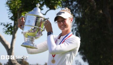 Nelly Korda, wearing a long-sleeved white top and white visor and with a gold medal on a red, white and blue ribbon around her neck, smiles and poses with the silver trophy, holding it up to her right