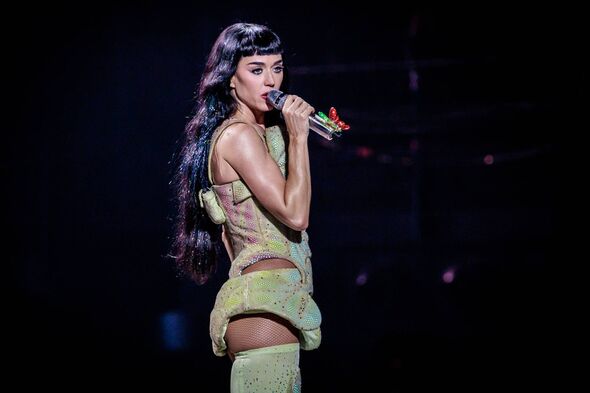 A female performer on stage under a spotlight, holding a microphone and singing, wearing a sleeveless dress.
