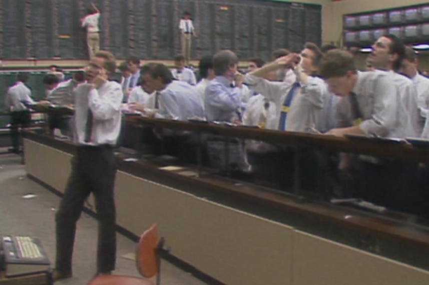 Men in shirts and ties shout while standing on a trading floor.
