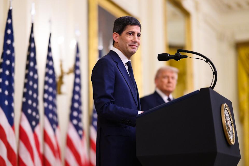 New Fed Chair Kevin Warsh standing at a podium with President Trump to his side.