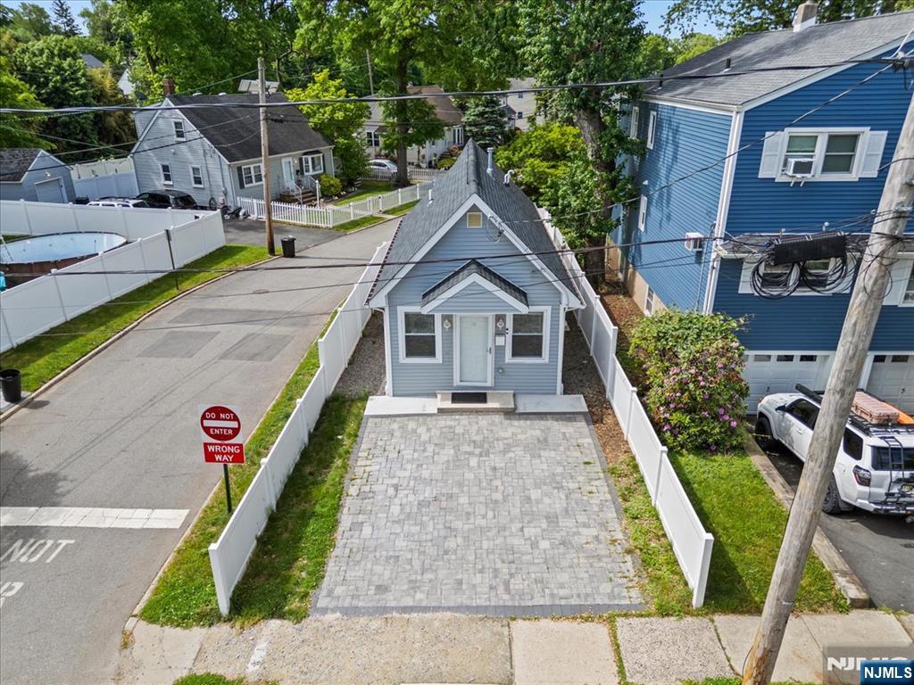 Small gray house with white trim and a paved driveway, with a blue house on the right and a street on the left.