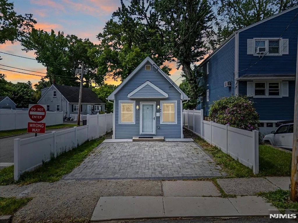 A small blue house with a gray paved driveway, and a white fence under an orange and blue sky.