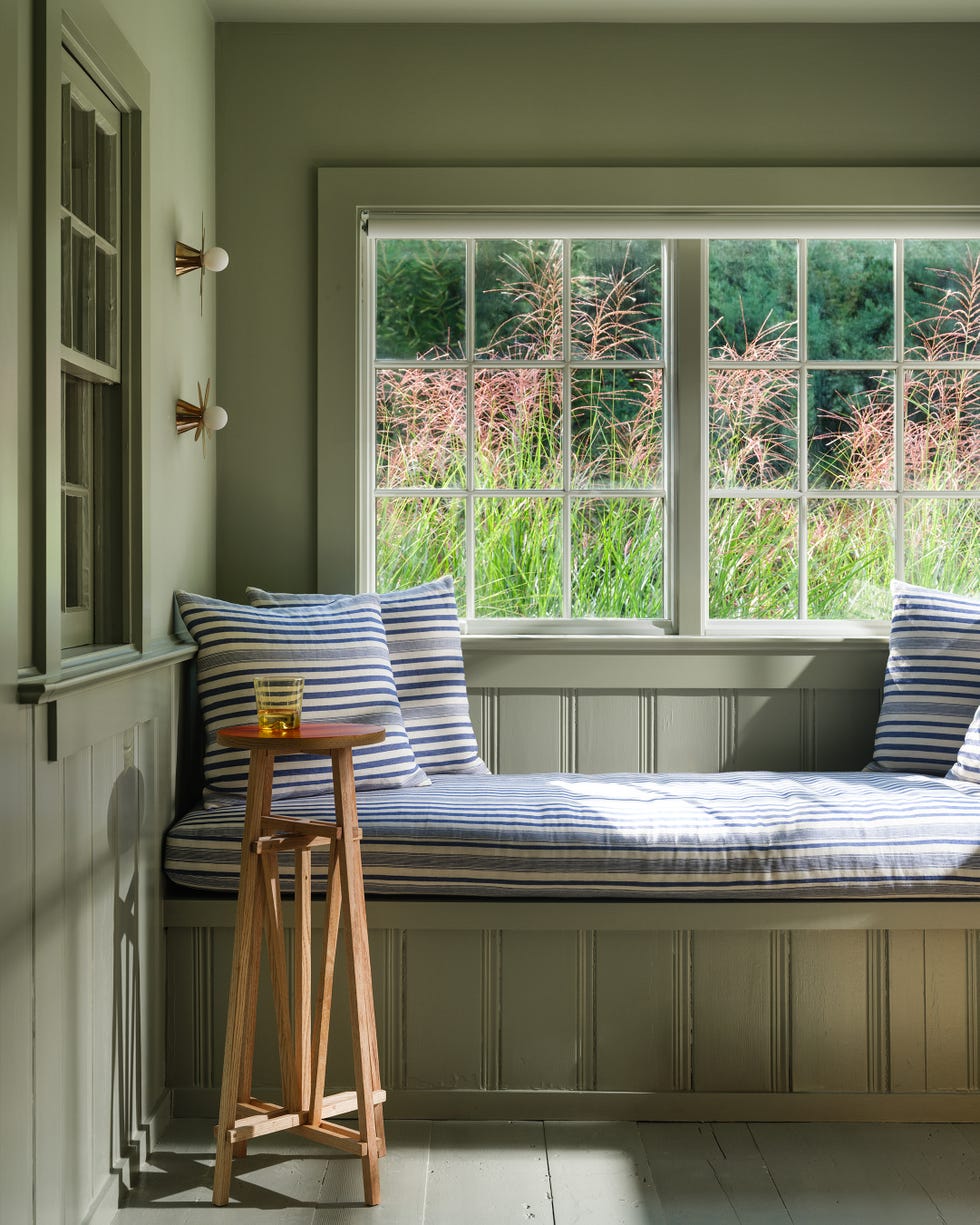 Cozy reading nook with striped cushions, small table, and garden view.