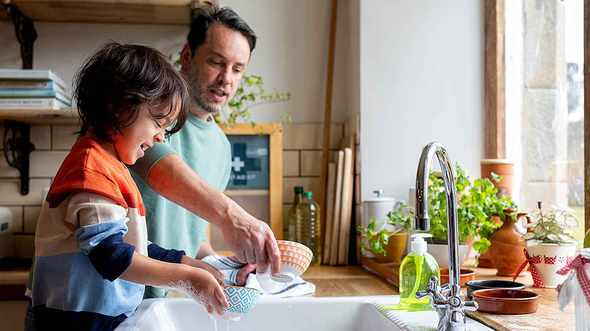 child and his dad washing and drying dishes together in their home