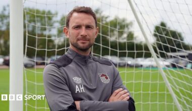Alex Hughes posing for a picture while stood in a goal wearing a Grimsby Town tracksuit