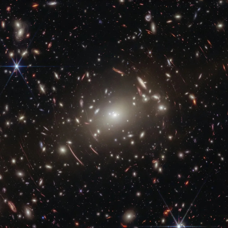 A view of lots of gravitationally lensed galaxies against the dark background of space.