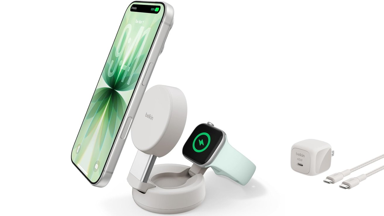 White multi-device wireless charging stand holding a smartphone and smartwatch, with a separate USB power adapter and charging cable placed to the right on a plain background