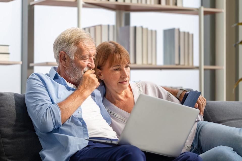 Senior couple spending time together in the living room, woman and man using laptop and digital tablet on the cozy sofa at home