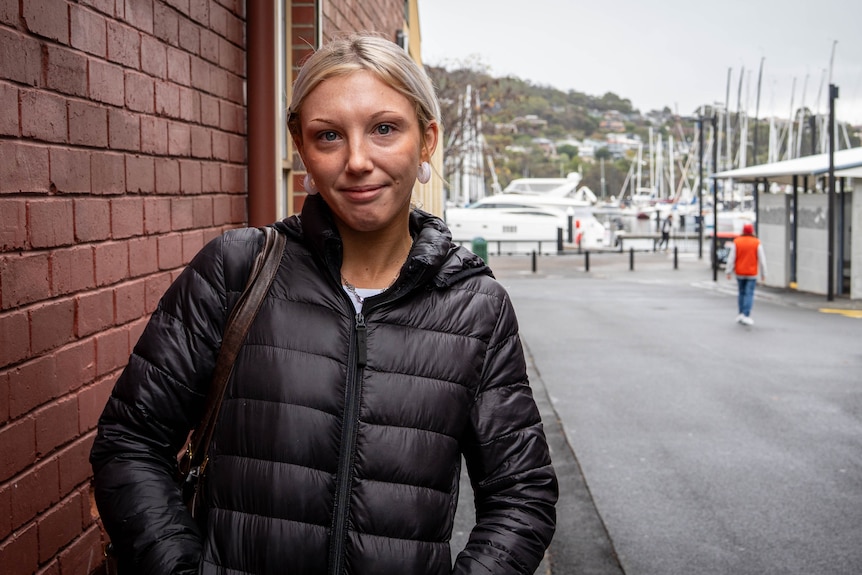 Woman standing in front of a brick wall leading to a dock full of boats.