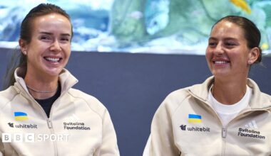 Elina Svitolina and Marta Kostyuk sit together and smile wearing cream zip-up jackets
