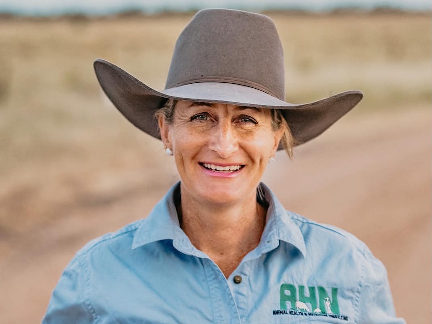 A woman in a brown felt hat smiles to camera