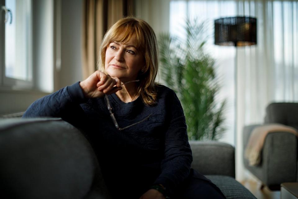 A person sitting on a couch, looking off and thinking.