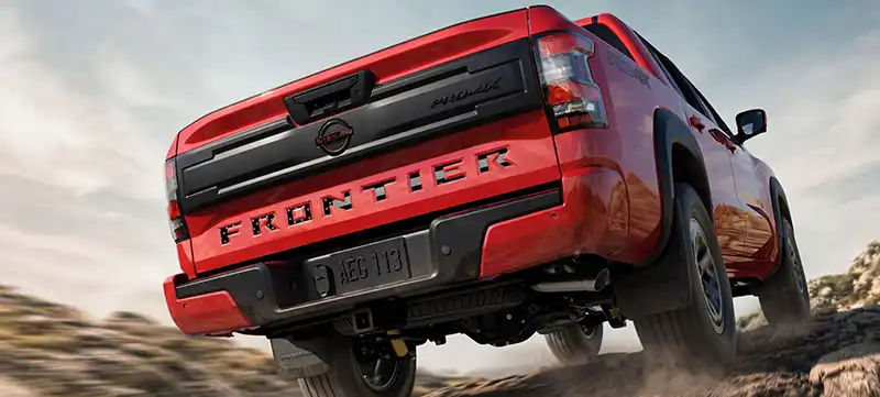 Wide rear angle of the 2026 Nissan Frontier driving over a dirth path