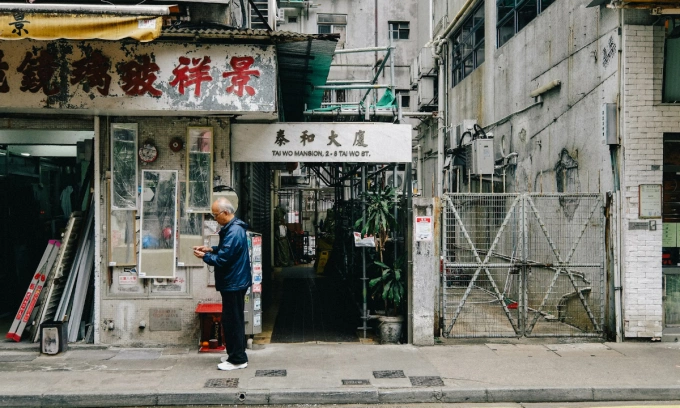 An elderly man stands on a street with old buildings in Hong Kong. Photo by Unsplash/Andy Thanh Hai