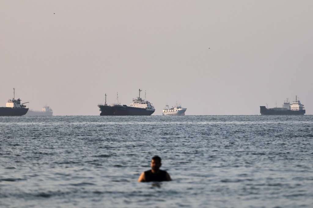 A person stands on shallow water as cargo and commercial vessels are anchored in the Strait of Hormuz off Bandar Abbas, Iran, Monday, June 8, 2026. (Amirhosein Khorgooi/ISNA via AP)
