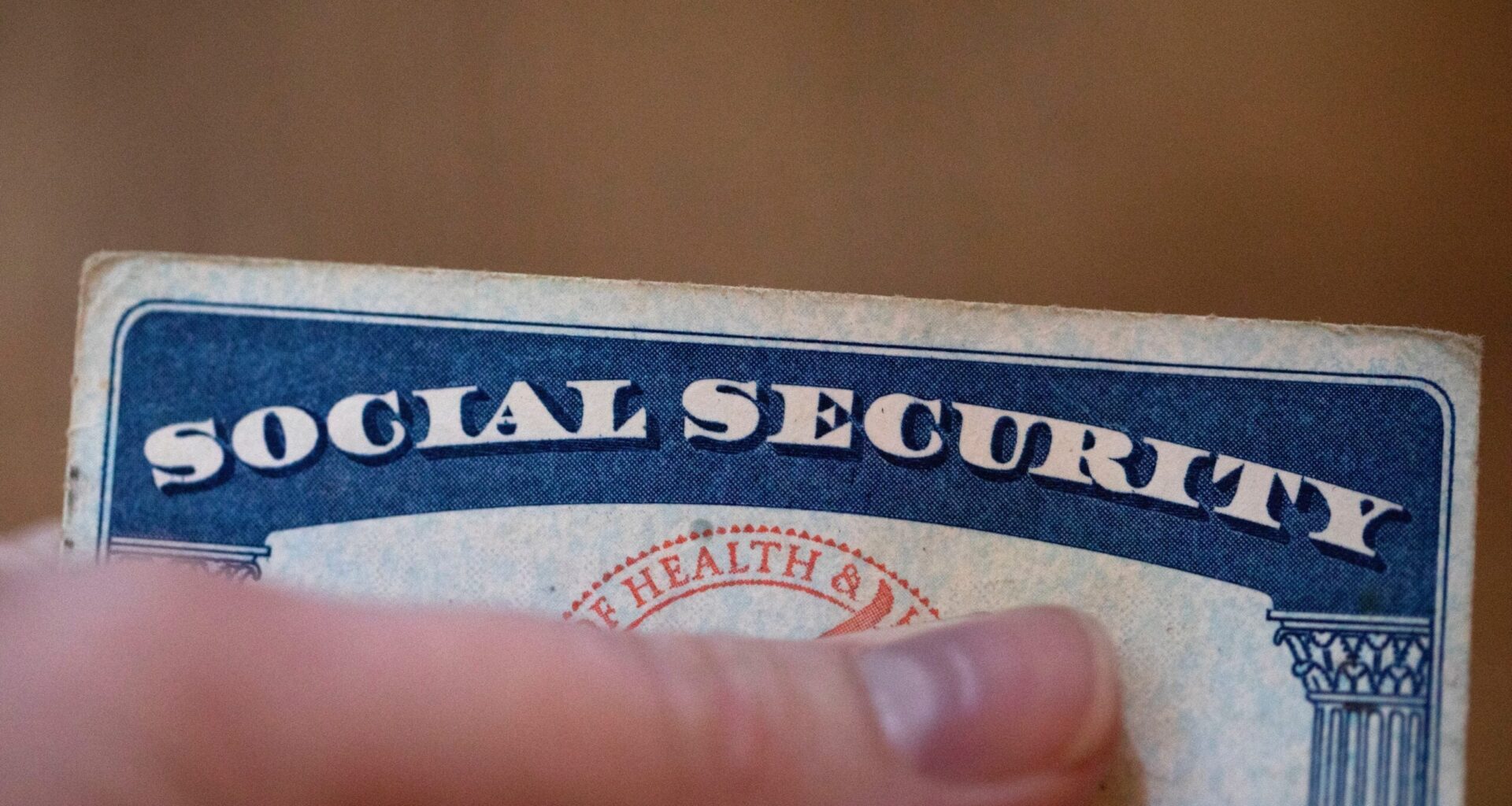 A hand holding the top edge of a Social Security card with the words Social Security clearly visible.