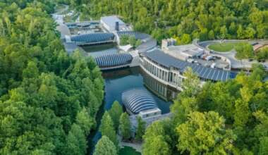 Aerial view of modern architecture museum surrounded by lush green forest and water in a scenic landscape.
