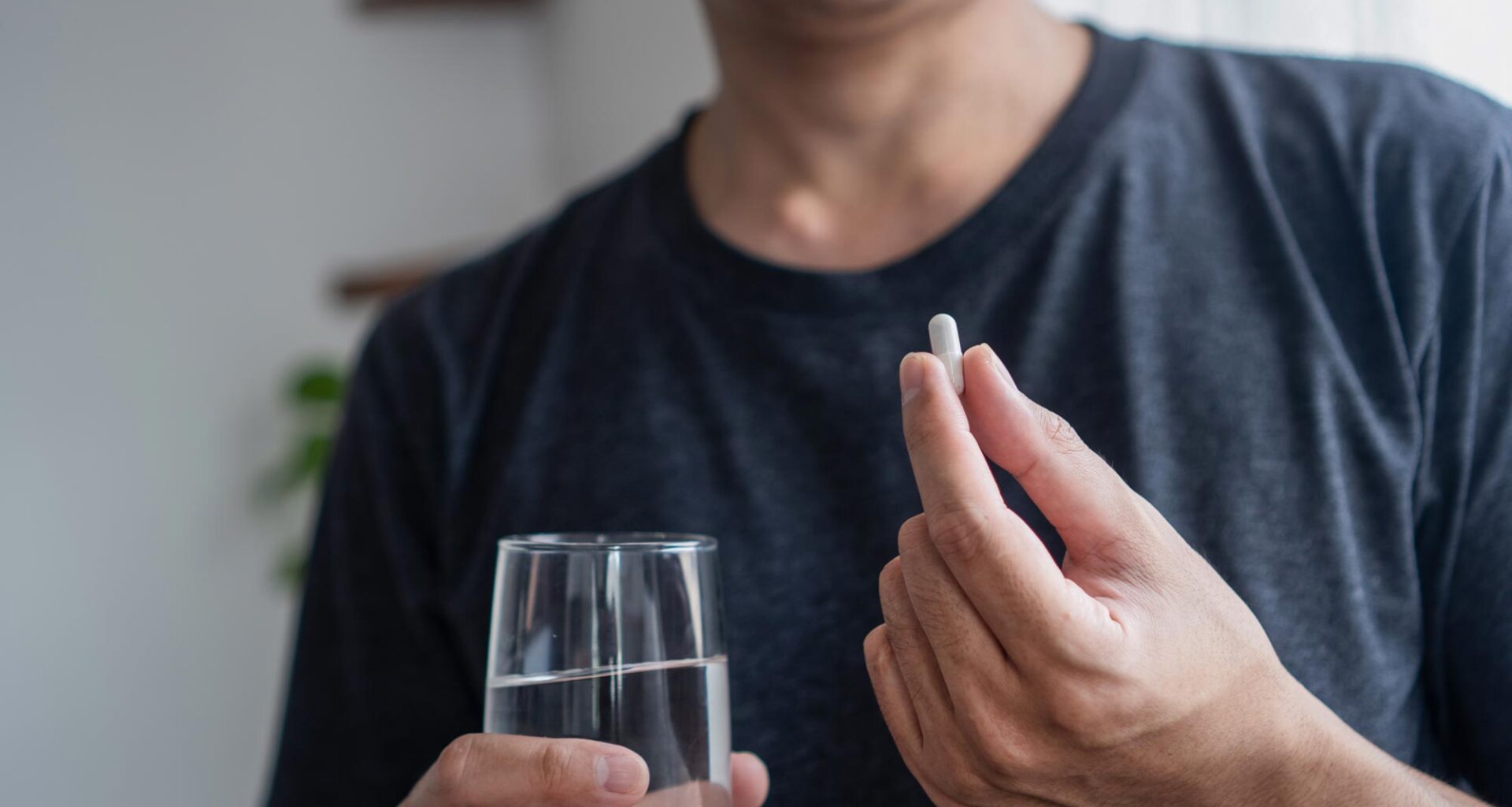 Asian Man Taking Supplement Capsule Pill With Water