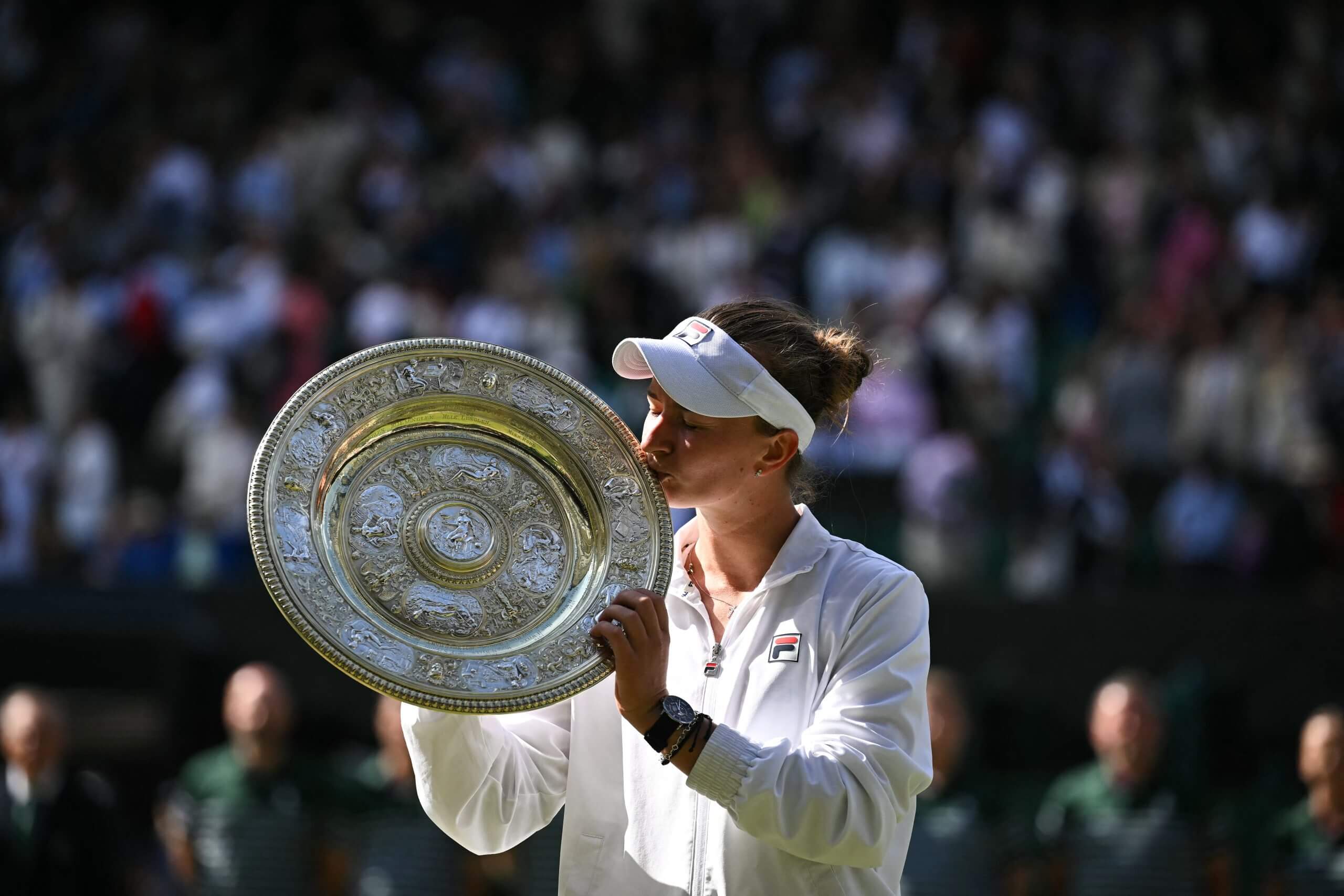 Barbora Krejčíková kisses the Venus Rosewater Dish, the women's singles trophy at Wimbledon, with a crowd behind her.