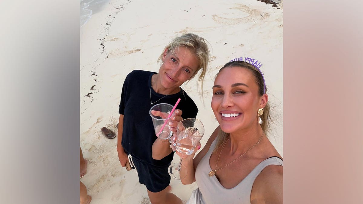 Brittany Aldean smiles with a friend while holding a drink and wearing a purple 