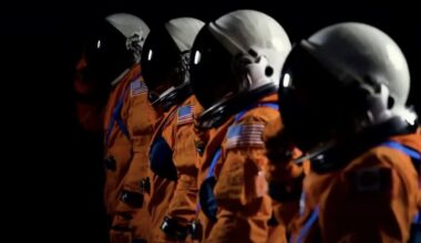 four spacesuits stand with white helmets.